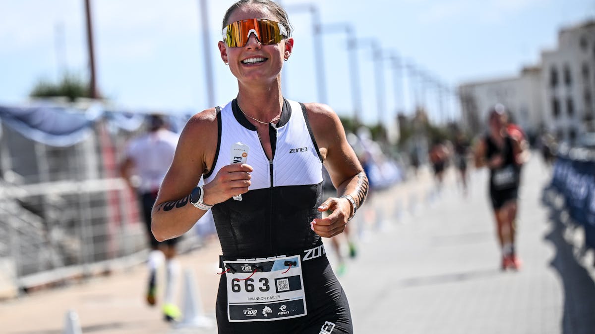 A person wearing a trisuit and sunnies whilst on the run leg of their triathlon race.