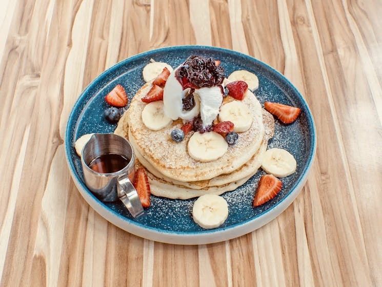 A plate of pancakes with fruit and syrup on the side
