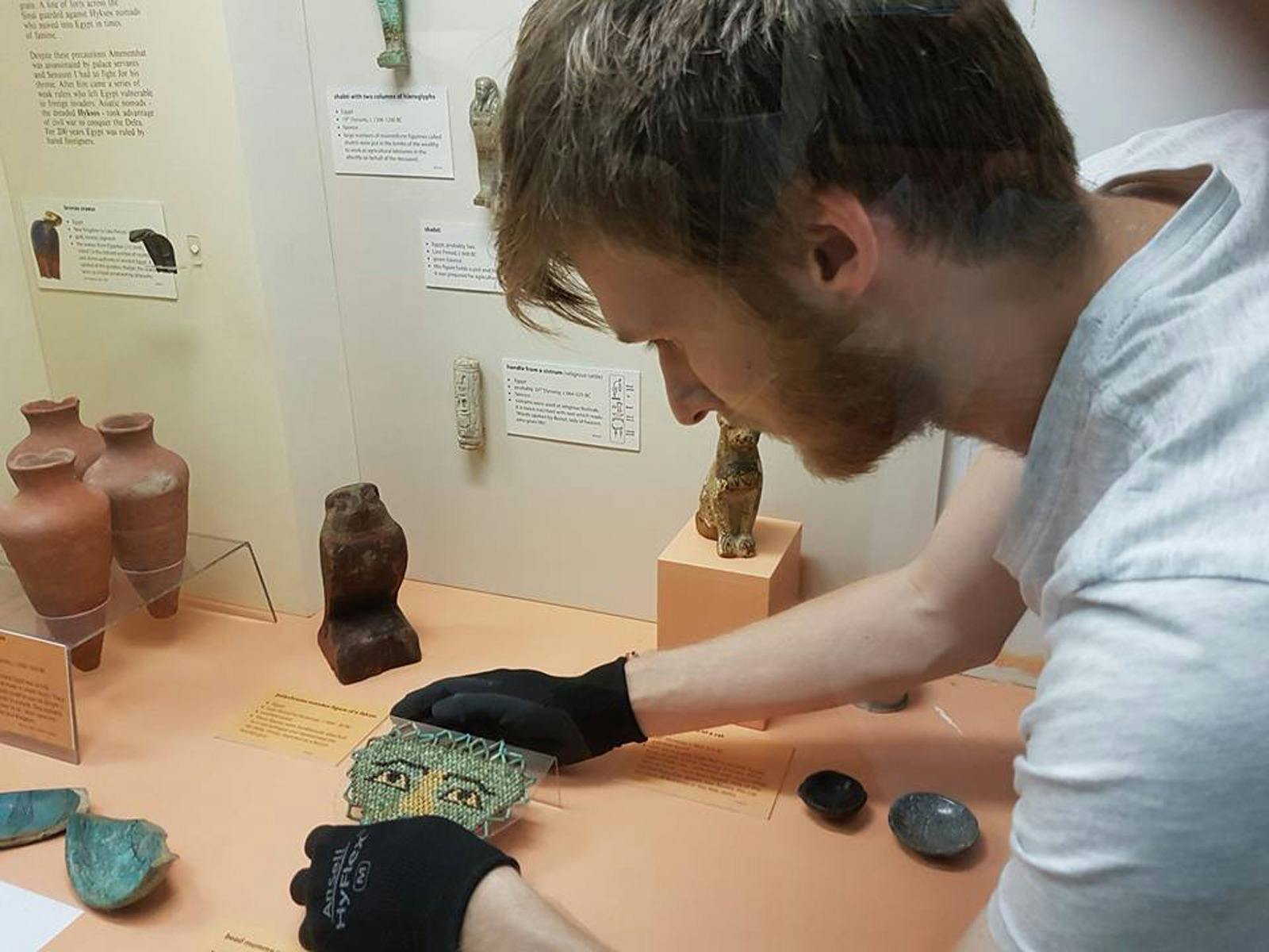 A view into the Egyptian Display Case showing staff with gloves arranging artefacts and  labels .