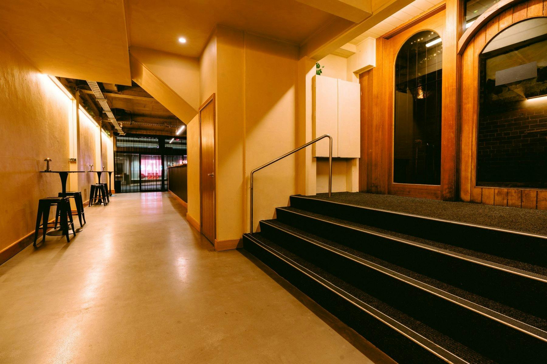 Interior hallway with stairs, bar stools, and warm lighting leading to a bar area.