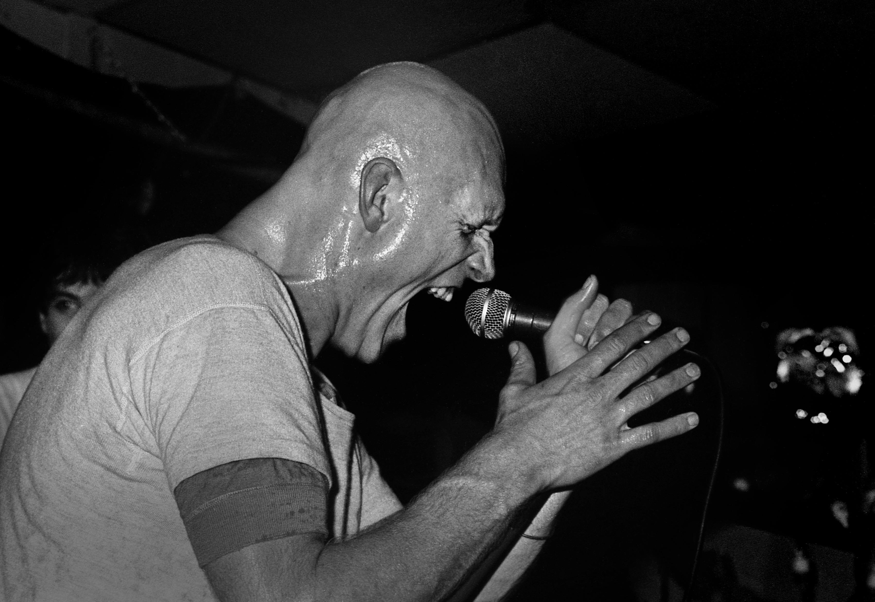 tall bald man sings into a microphone with great energy and passion