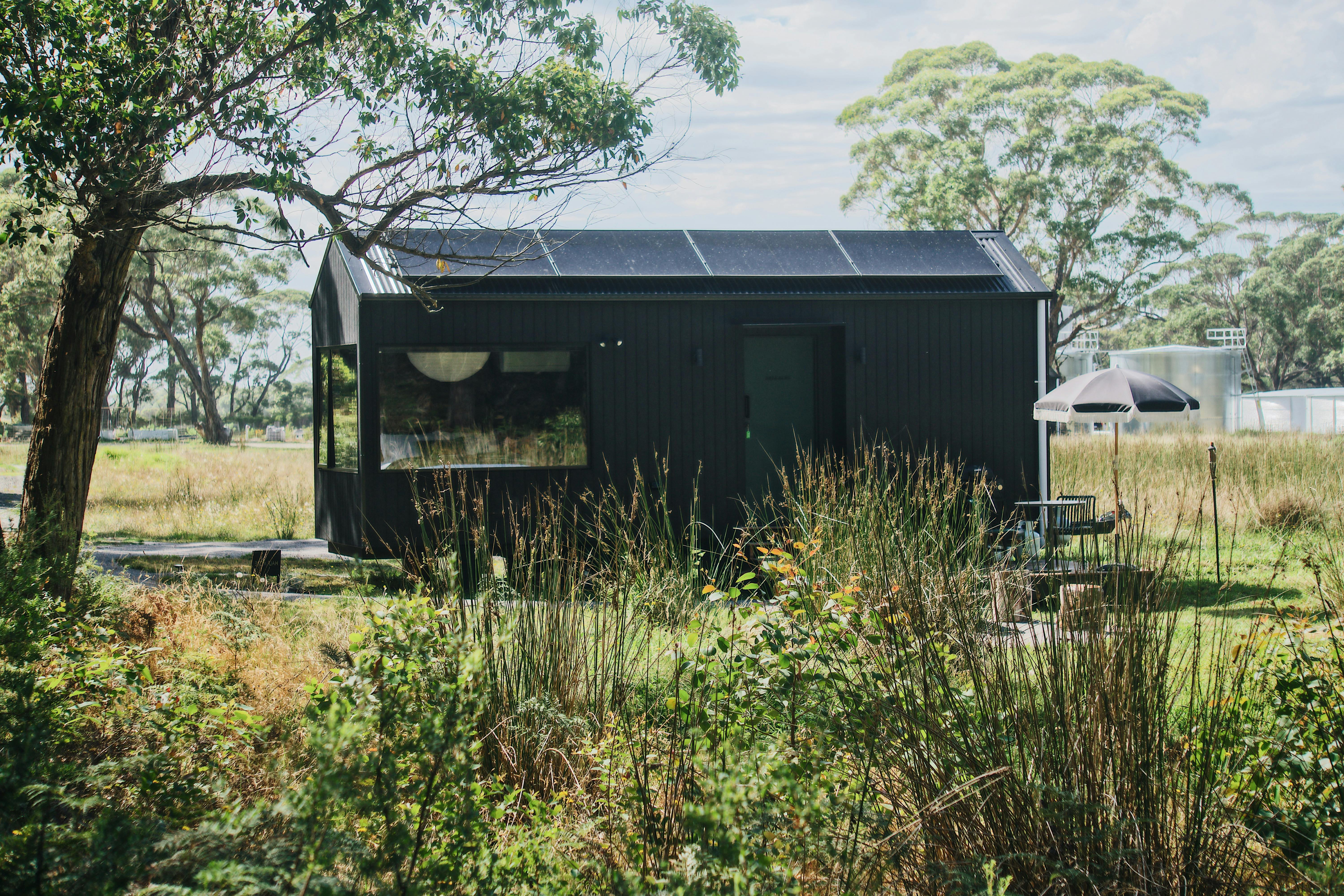 A black tiny home sitting amongst native bush