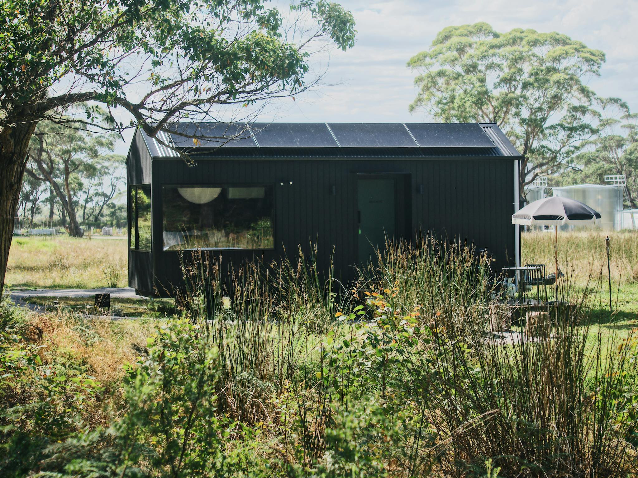 A black tiny home sitting amongst native bush