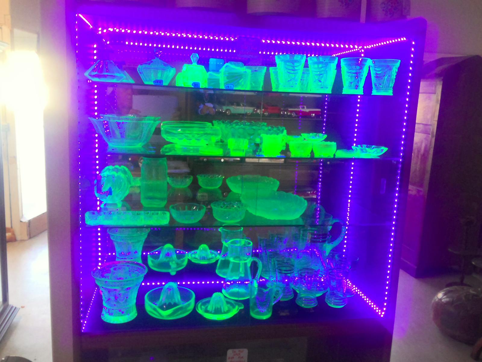 A cabinet of glassware illuminated with UV light showing glassware
