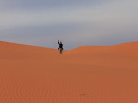 Man waving to the camera on a huge red sand dune