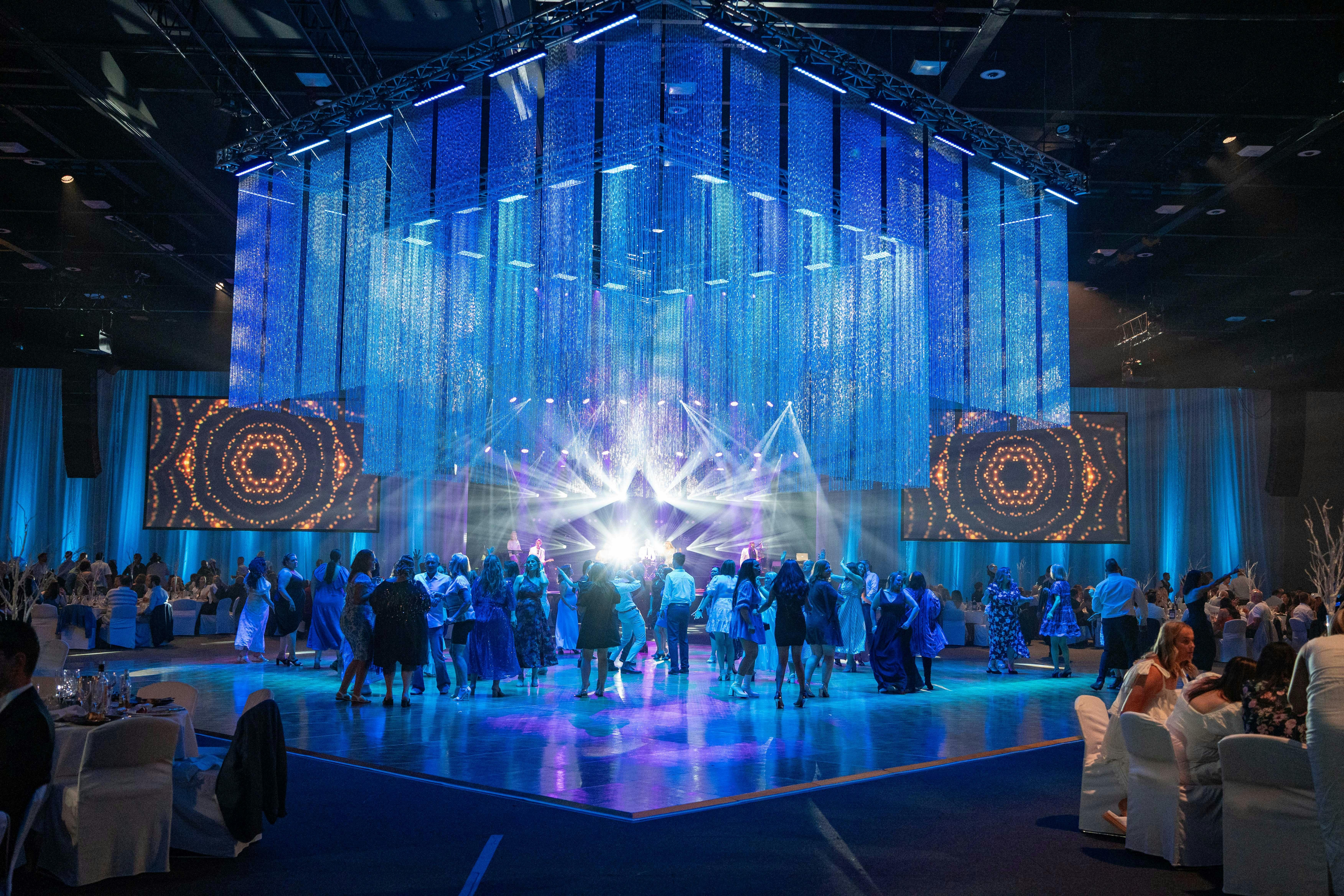 Image of an event hall with people on the dancefloor, underneath a chandelier with blue lighting