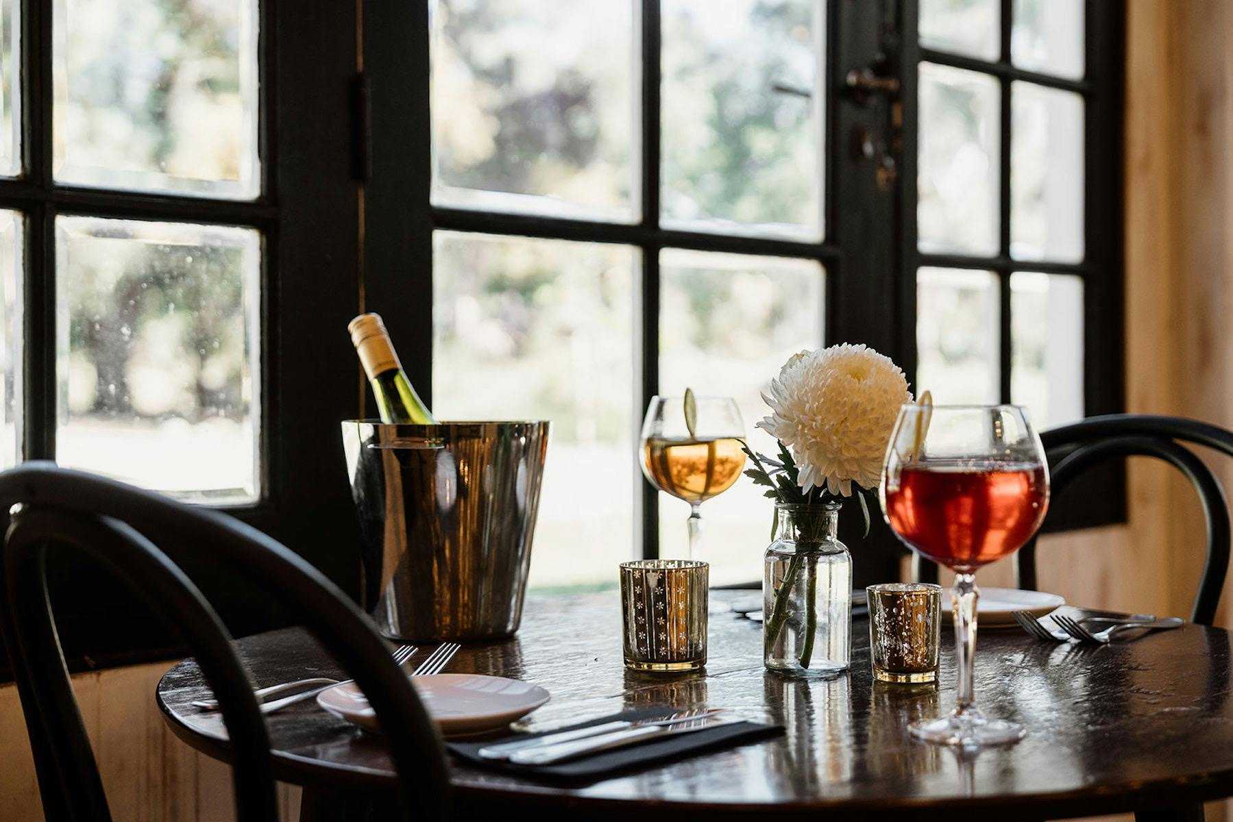 A table set for 2 guests with a bottle of wine in a wine bucket, 2 drinks already poured.