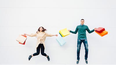 A man and a women holding shopping bags jumping in the air and smiling.
