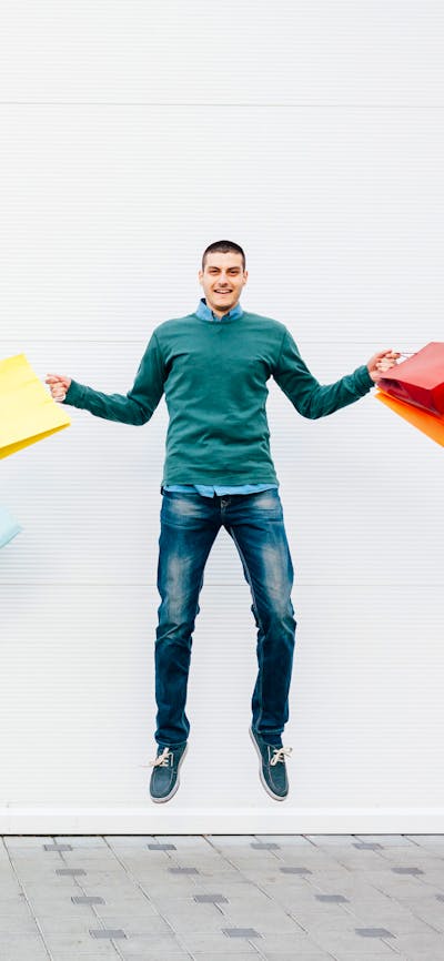 A man and a women holding shopping bags jumping in the air and smiling.