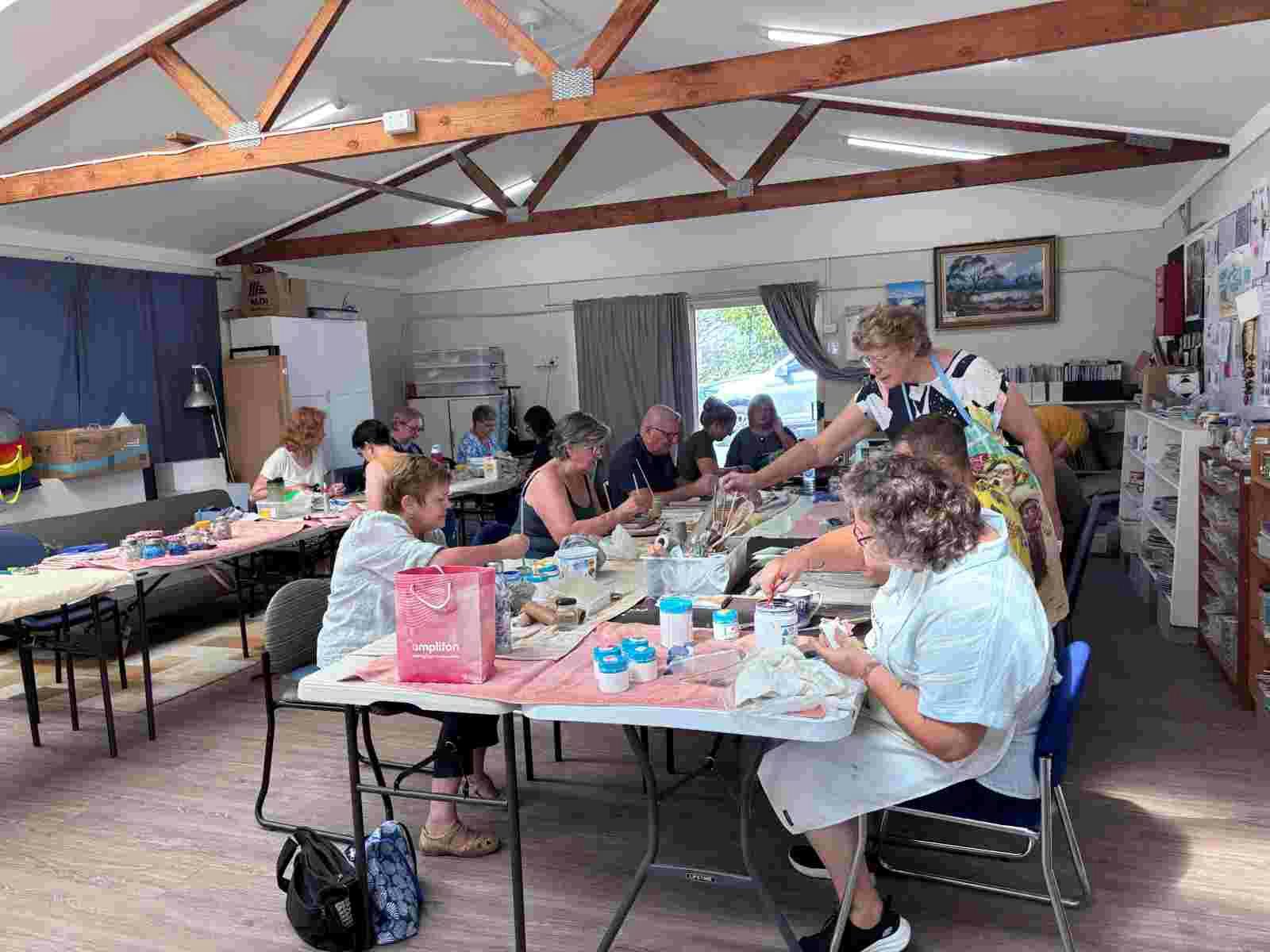 A group of people sitting at tables working on the pottery pieces