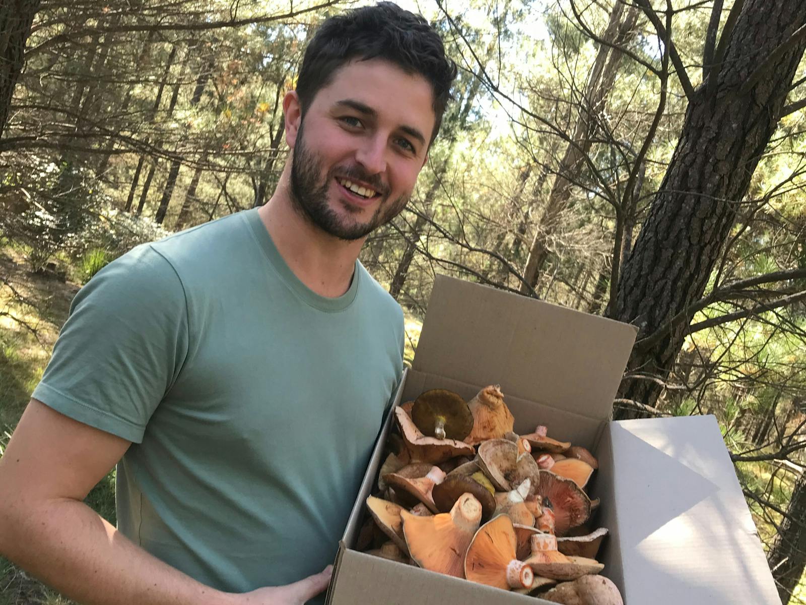 a youing man holding a cardboard box full of mushrooms