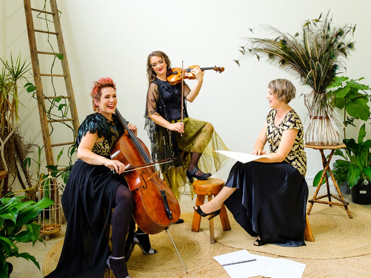 The three members of Muses Trio pose against a backdrop with fauna and a ladder.