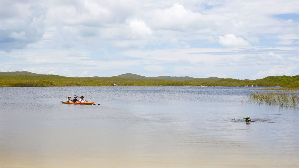Three people in a red and yellow kayak on a lagoon.