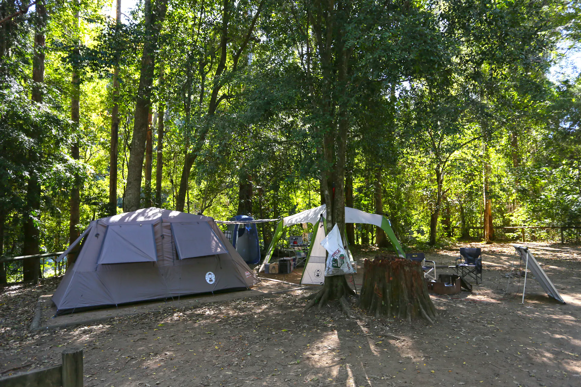 Tent and gazebo set up at camping area under shade of trees.