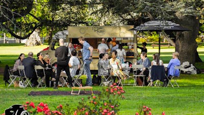 People standing and sitting on chairs and tables in front of van