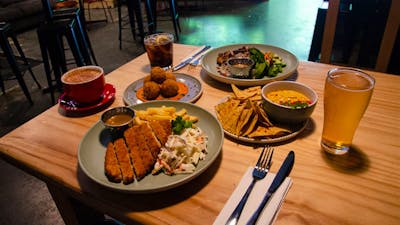 Variety of Dissent's food offerings set out on a wooden table. Arancini, schnitzel and corn chips.