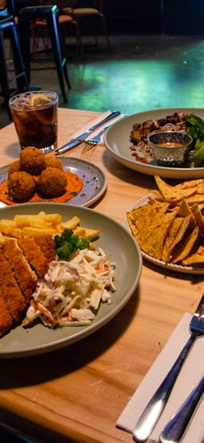Variety of Dissent's food offerings set out on a wooden table. Arancini, schnitzel and corn chips.