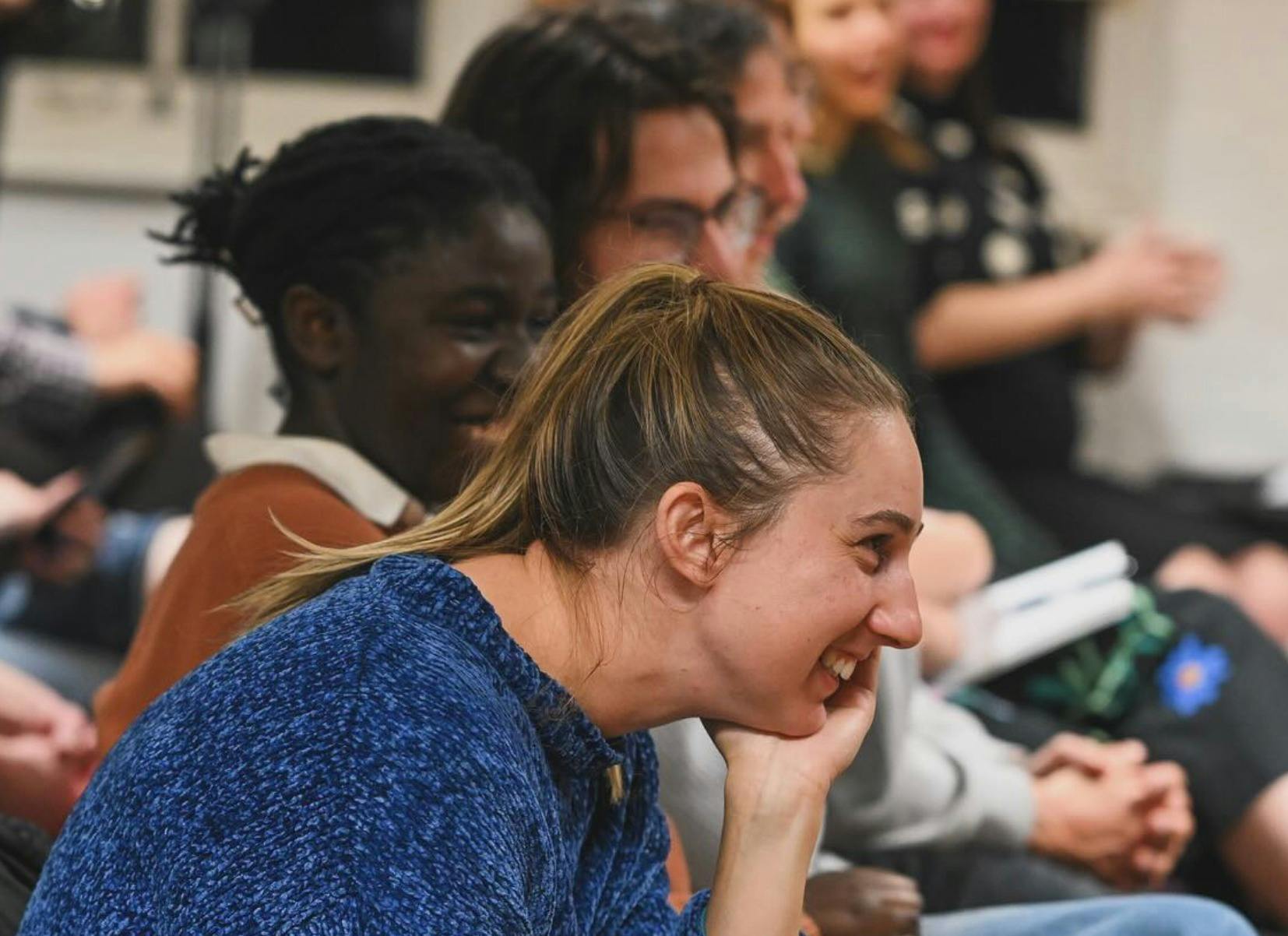 A photograph of a person sitting in an audience smiling