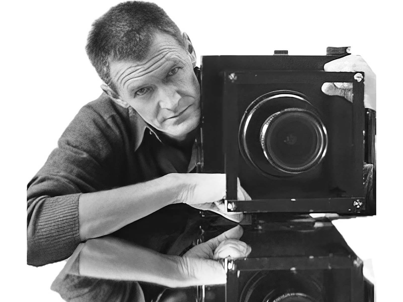 A black and white photo of John Gollings with a vintage black camera ready to take a photo.