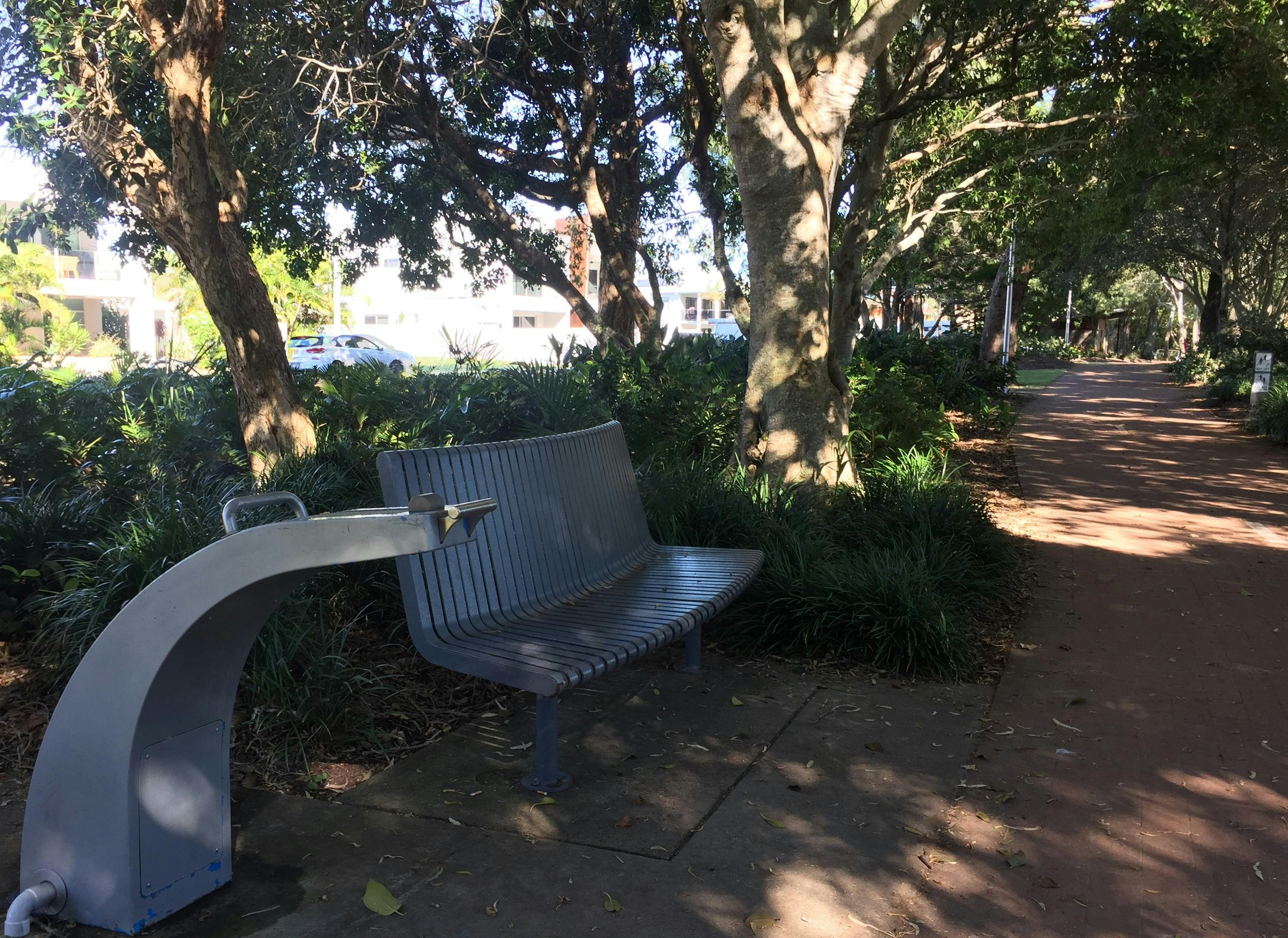 photo showing part of the Hervey Bay Coastal pathway with water station and bench seat under trees