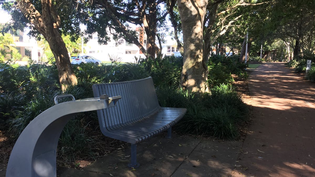 photo showing part of the Hervey Bay Coastal pathway with water station and bench seat under trees