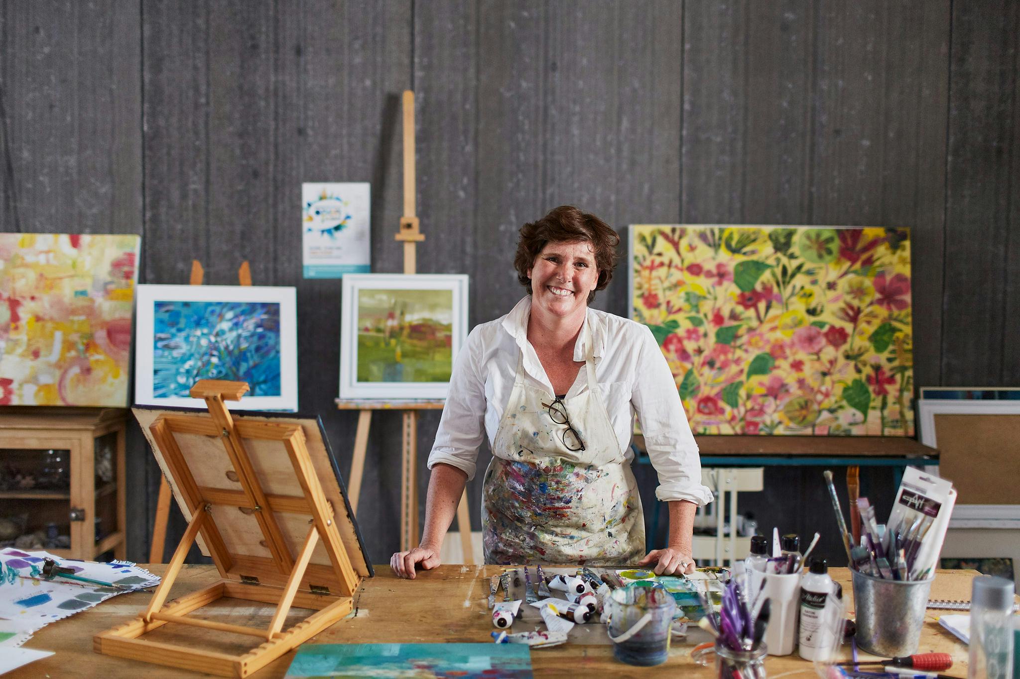 Smiling female artist surrounded by paintings