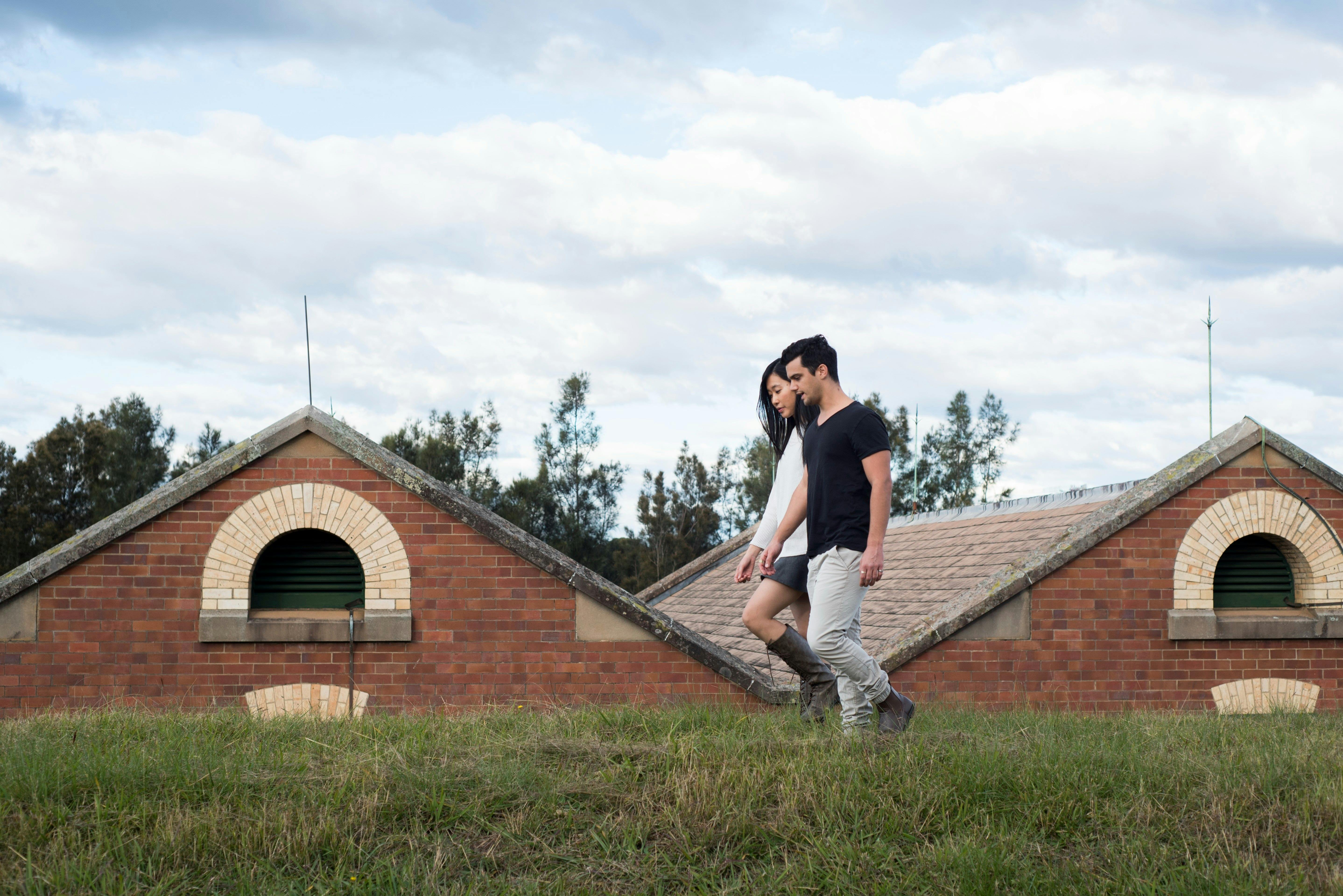 Zwei Personen gehen im Vordergrund eines denkmalgeschützten roten Backsteingebäudes mit Giebeldachlinie.