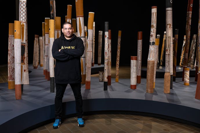 A man standing in a gallery space with indigenous poles