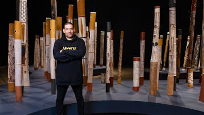 A man standing in a gallery space with indigenous poles