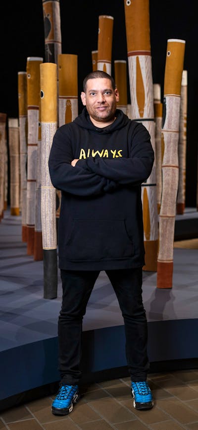 A man standing in a gallery space with indigenous poles