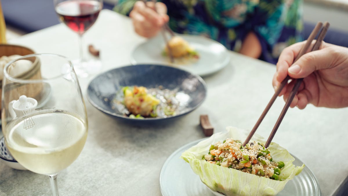 Man and woman at dinner eating san choy bow with chopsticks with a glass of wine each.