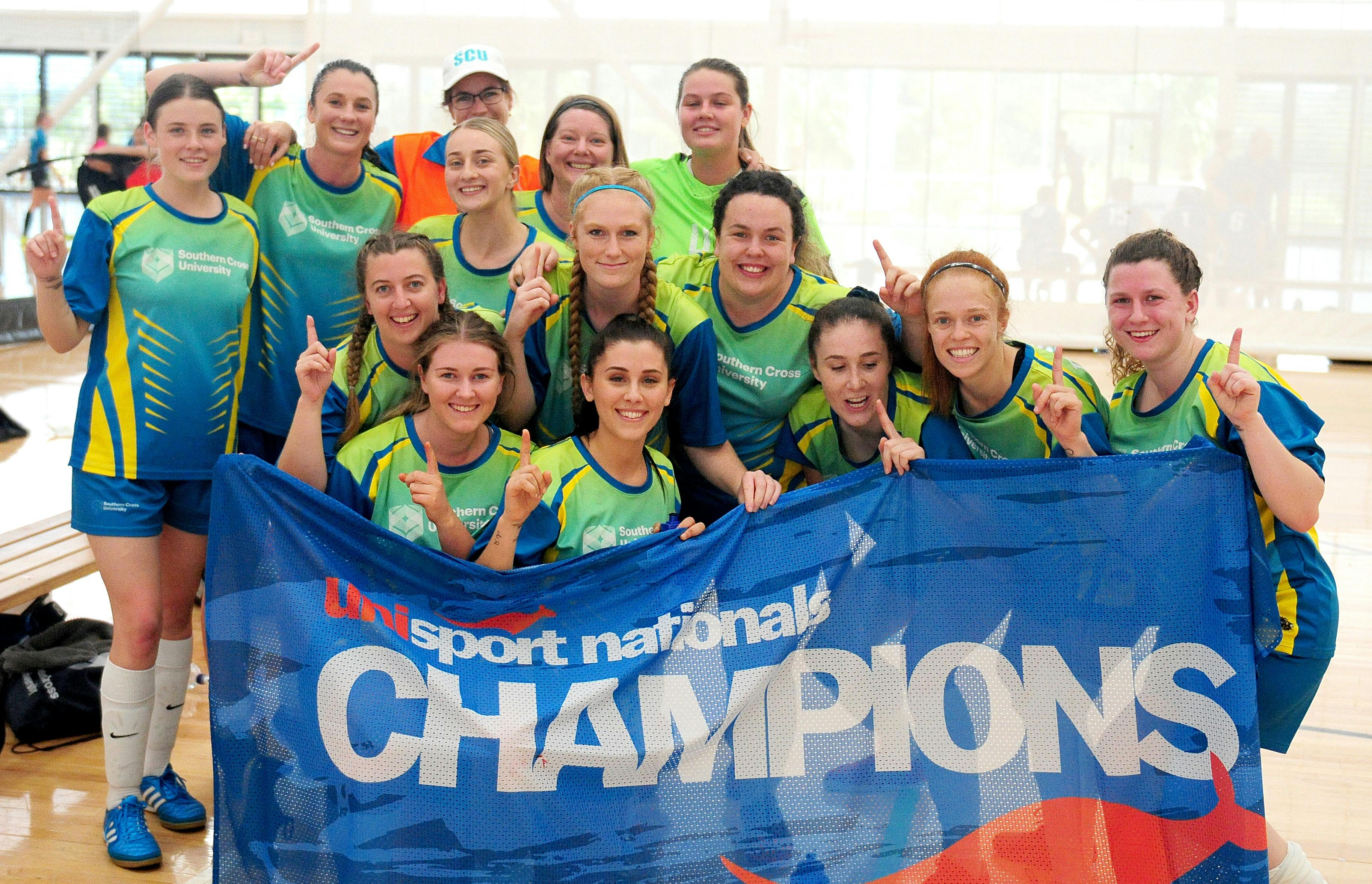 Women's futsal team posing with champion banner after winning 2019 Nationals