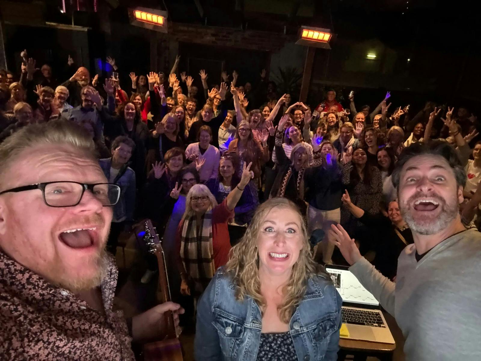 Selfie of three smiling performers onstage surrounded by a cheering, hands-raised crowd