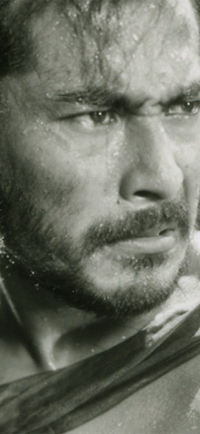 Black and white still of a man looking angry and a woman hiding behind the man