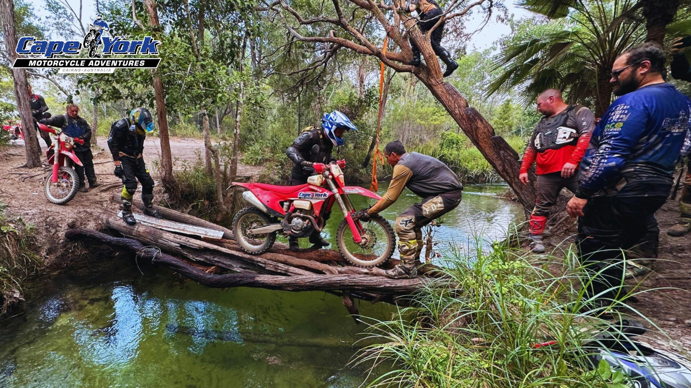 The team brings a motorcycle across a makeshift bridge.