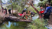 The team brings a motorcycle across a makeshift bridge.