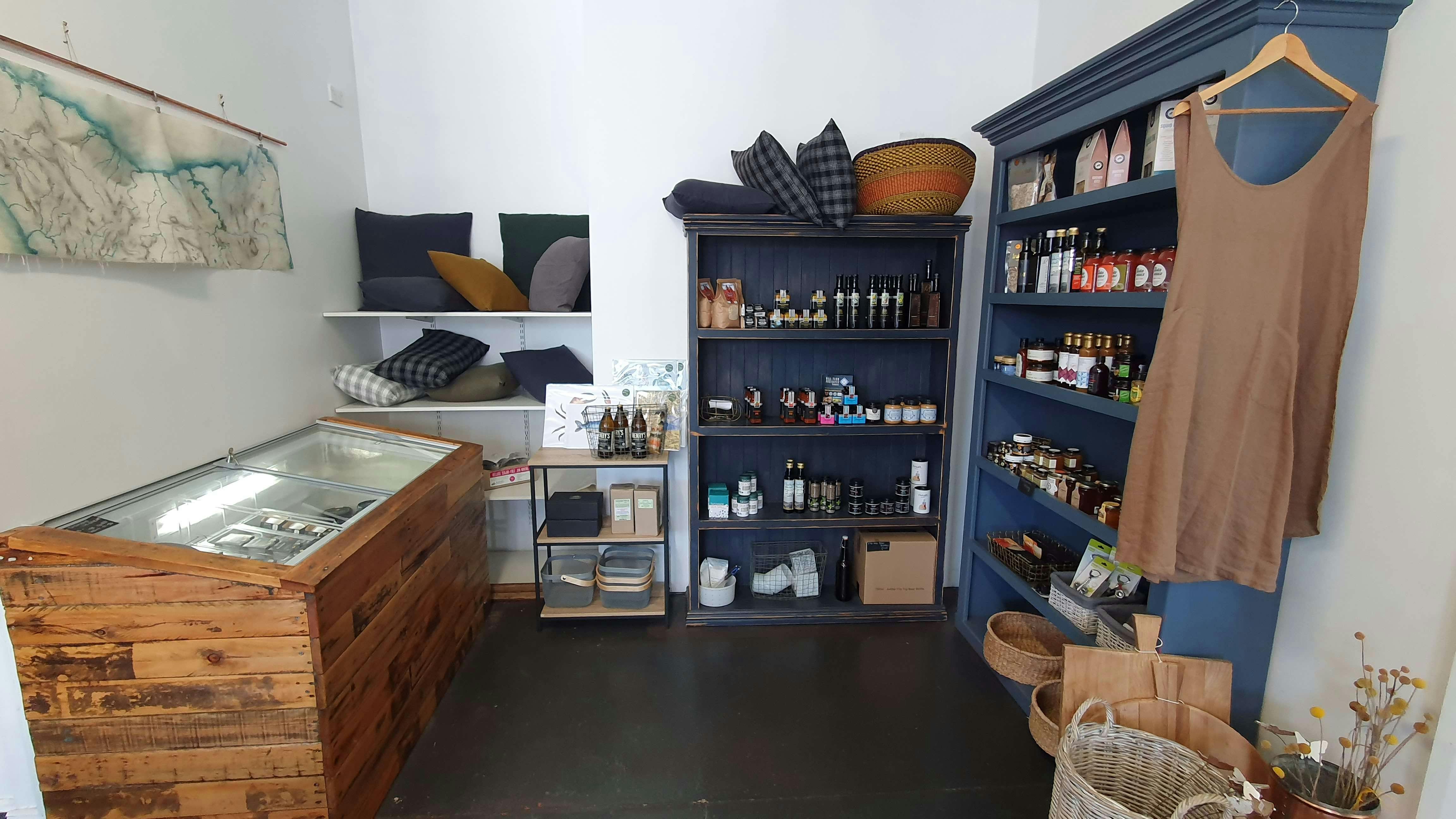 An inside of a shop, with blue shelves displaying food in jars and bottles, and a fridge