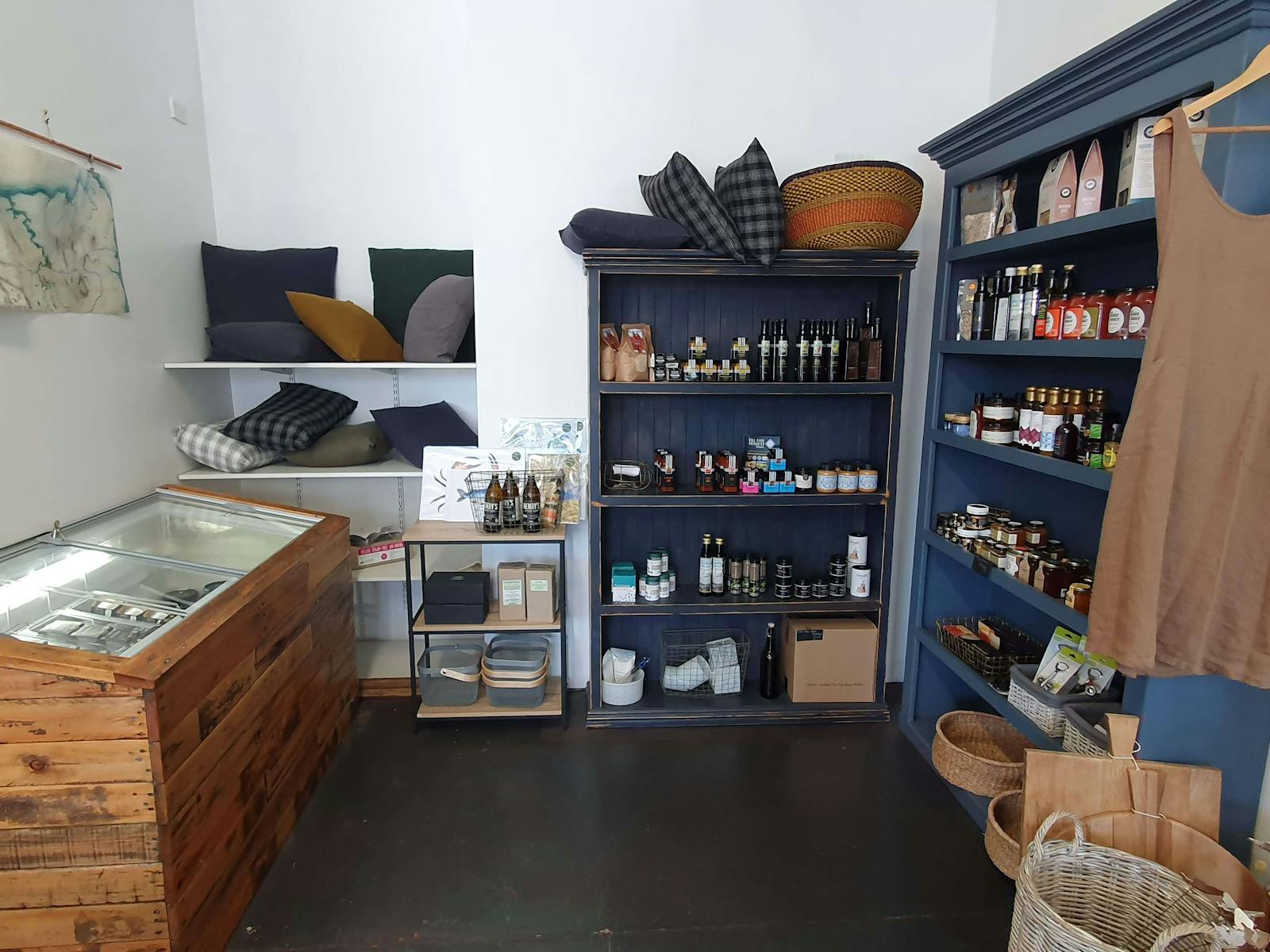 An inside of a shop, with blue shelves displaying food in jars and bottles, and a fridge