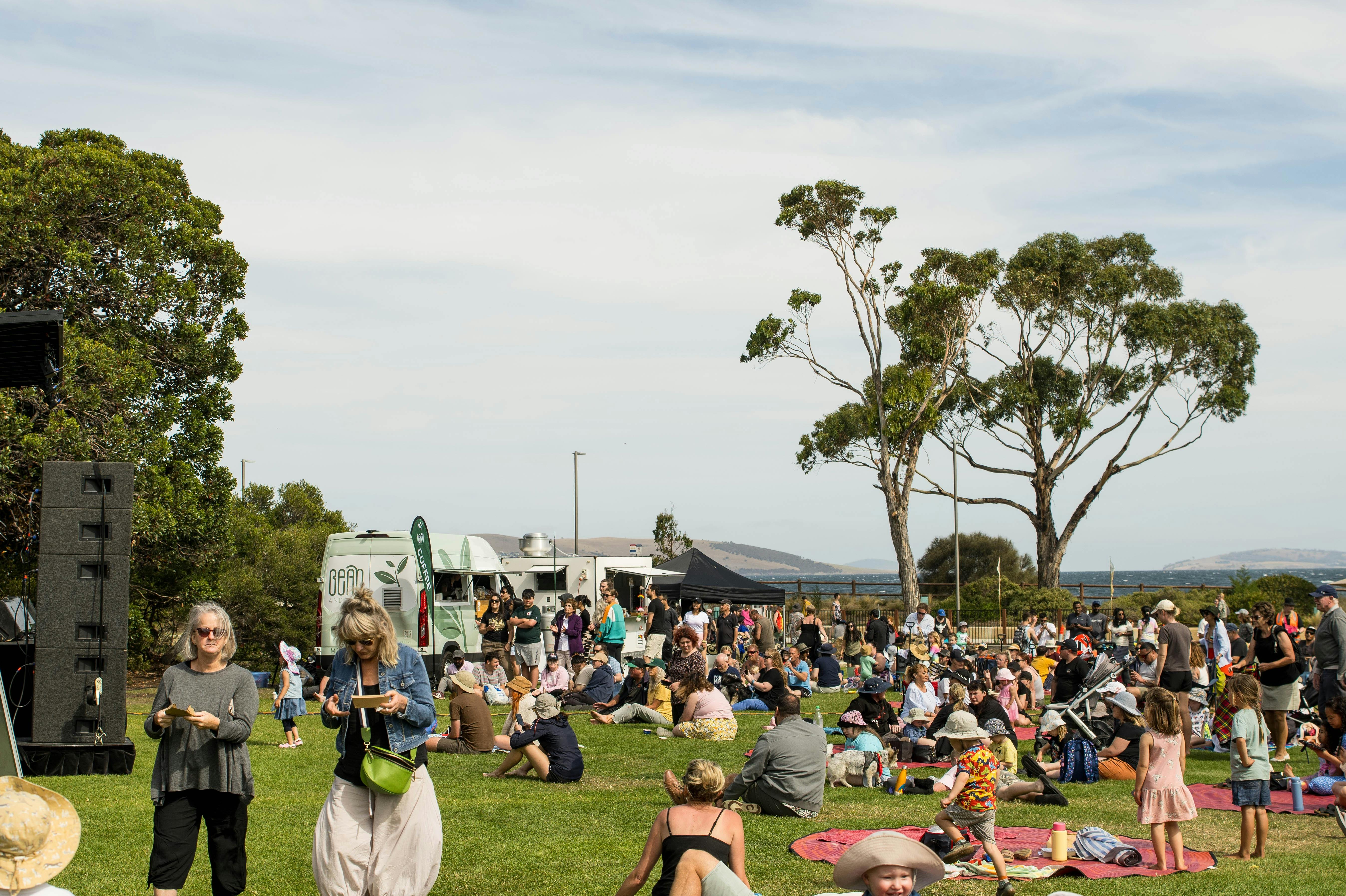Crowds of people sit and stand on grass at an event.