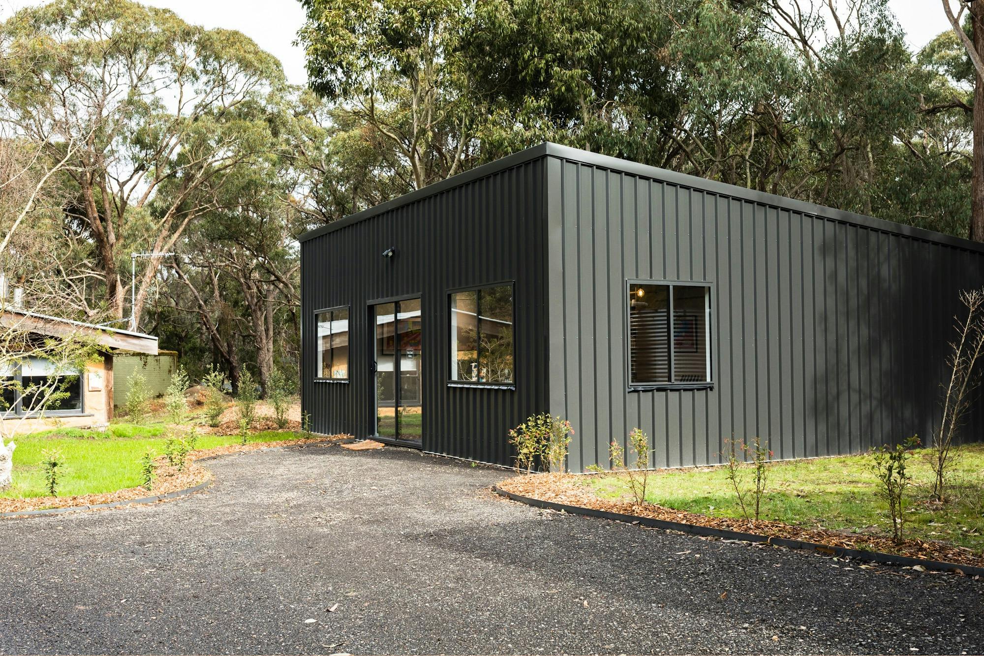 Black shed with 3 windows and sliding front door set in a green bush landscape