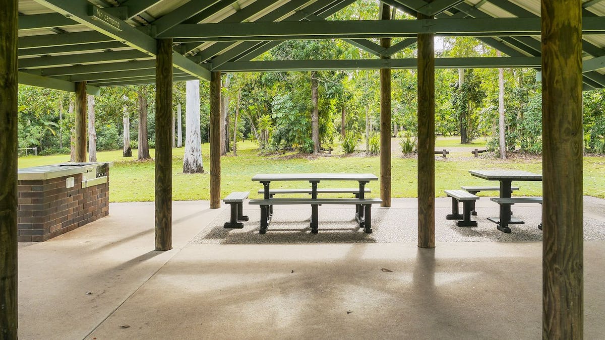 Picnic tables and barbeque on concrete under shelter with roof.
