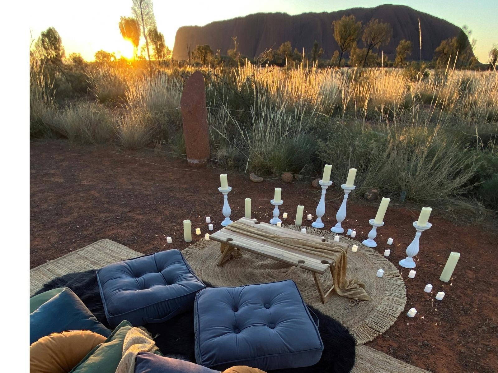 Picnic with rugs, cushions, throws and candles with Uluru in background