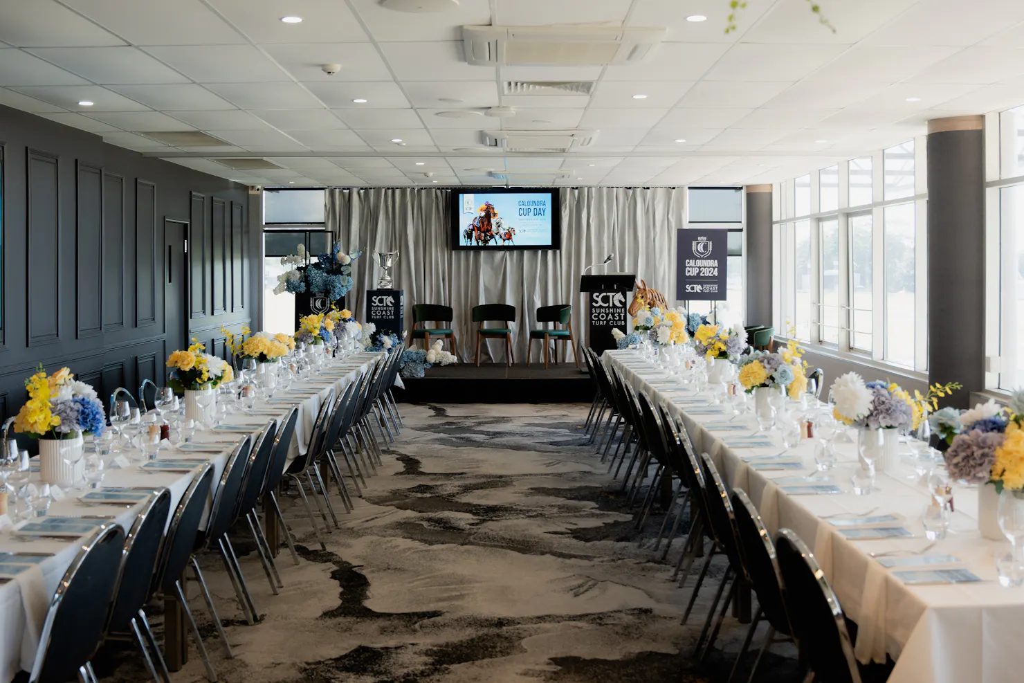 2 rows of long tables with a stage and chairs at the end ready for a business event