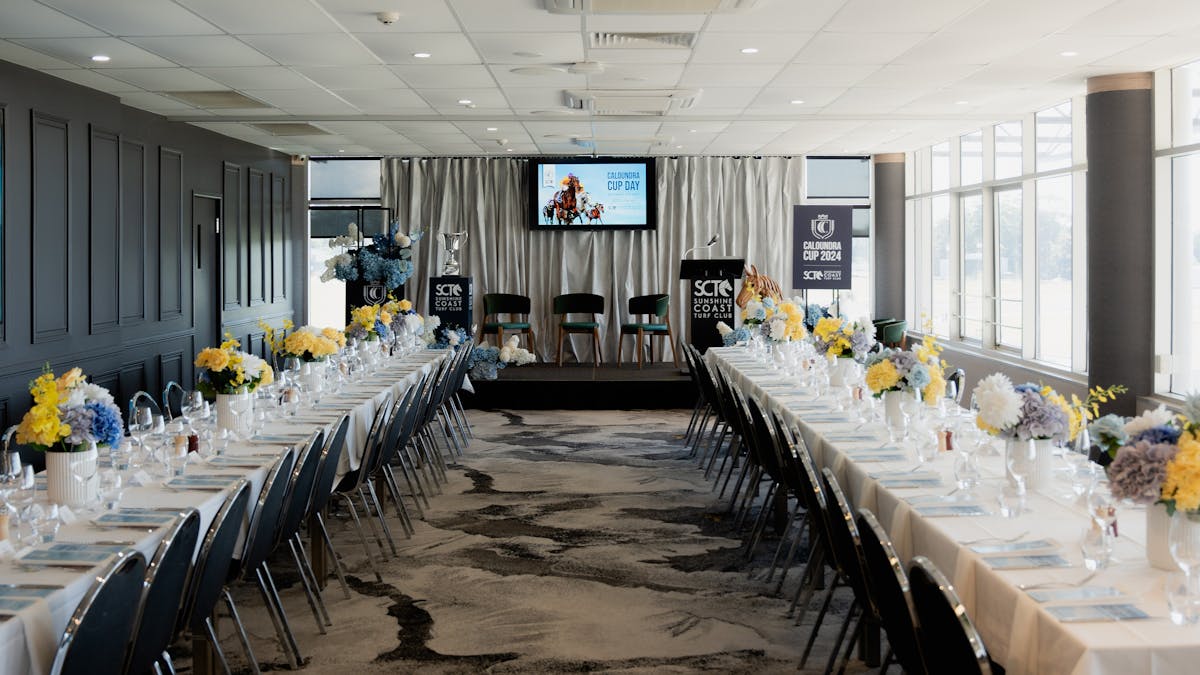 2 rows of long tables with a stage and chairs at the end ready for a business event