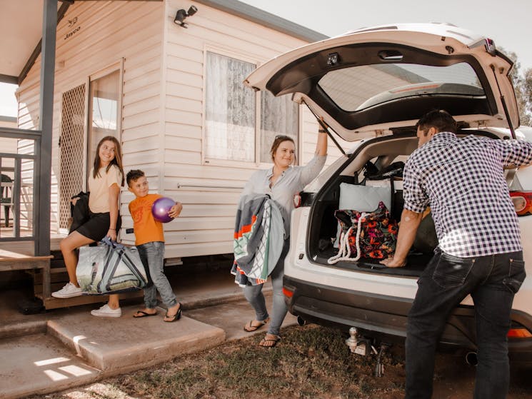 Family unpacking car to stay in caravan park cabin