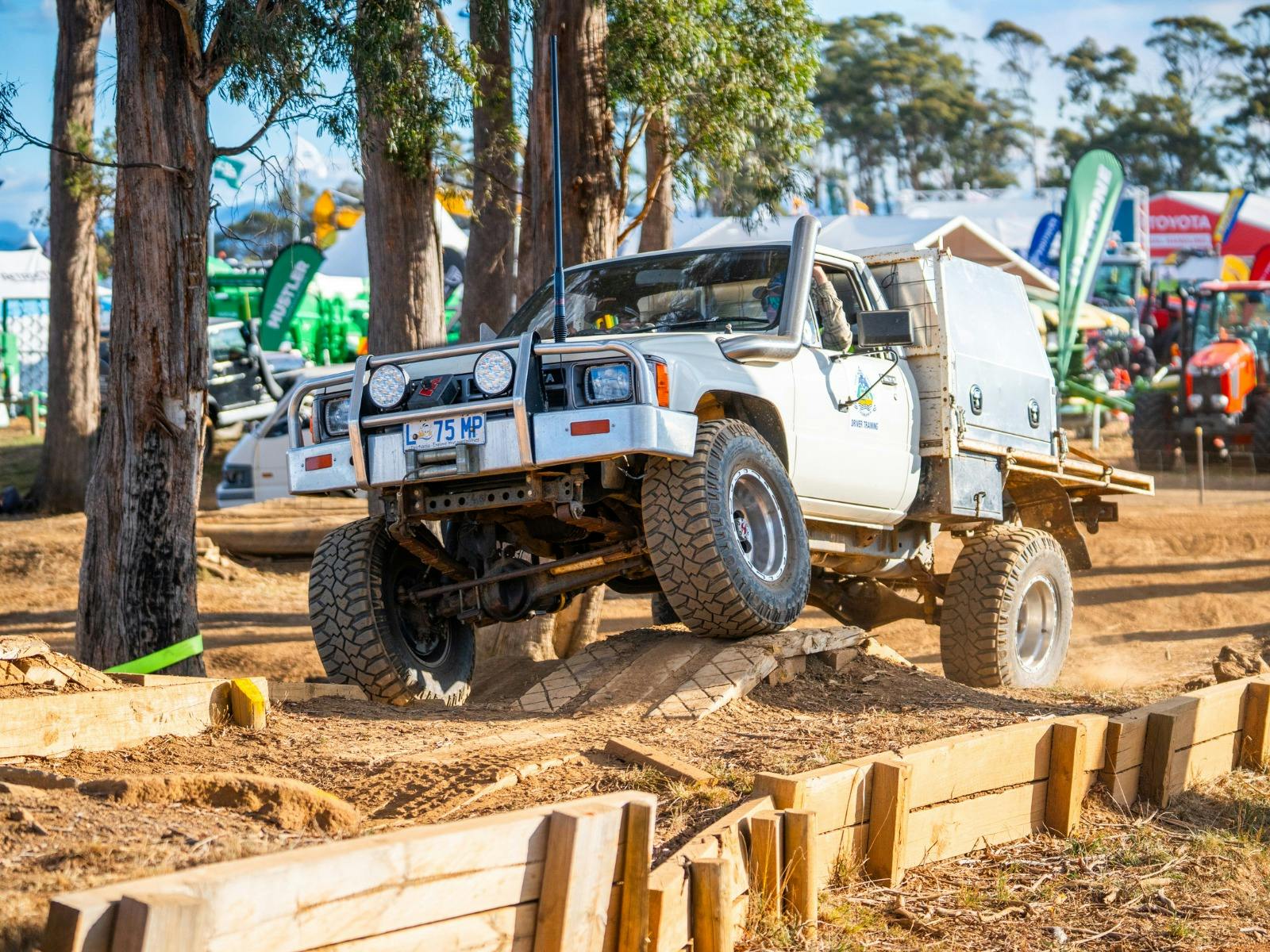 A 4WD ute tackles an off-road track, kicking up dust as spectators watch.