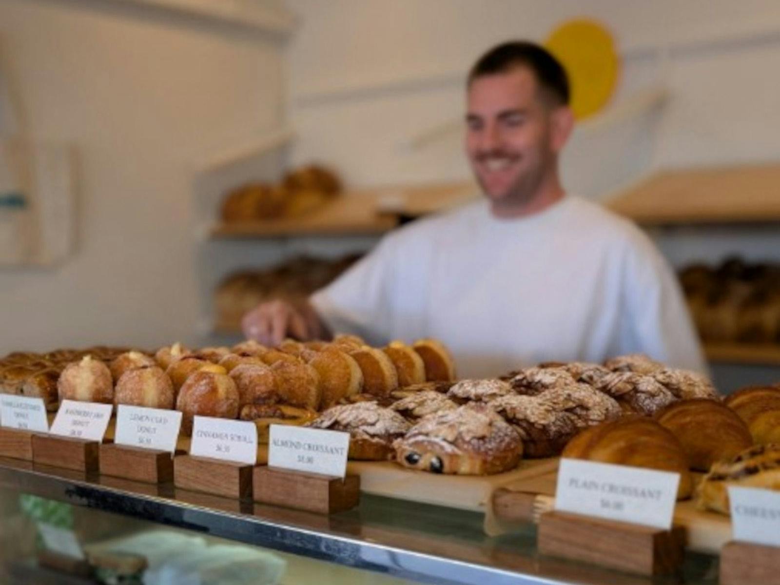 Man smiling behind counter full of bakery treats