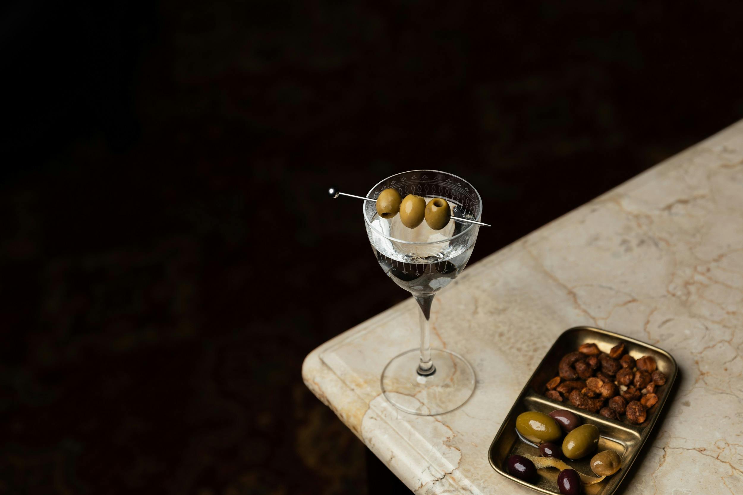 Martini on table next to plate of olives and nuts