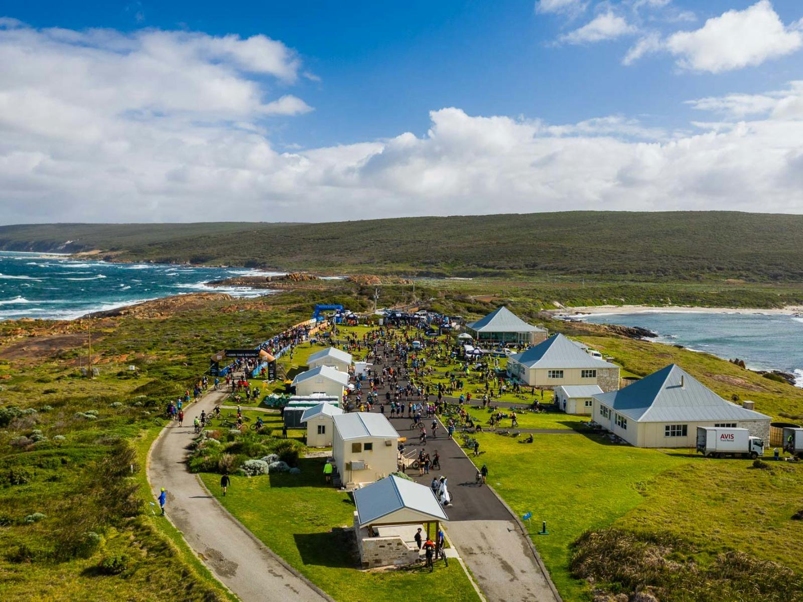 Drone aerial photo of Cape Leeuwin Lighthouse, coast in background, riders grouped around venue