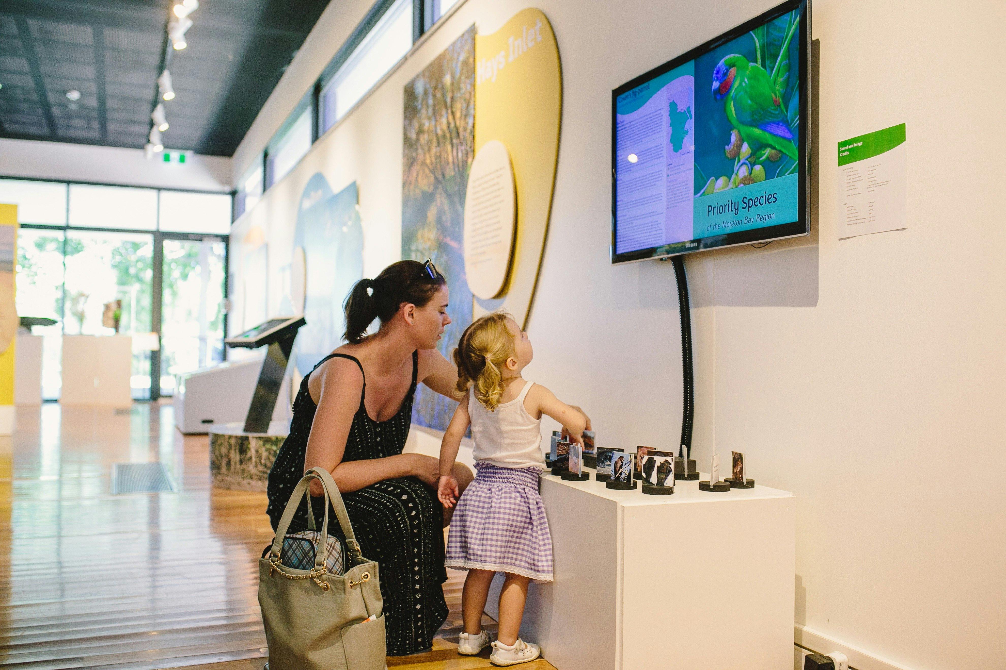 A girl and lady interactive with a exhibition item on bird species